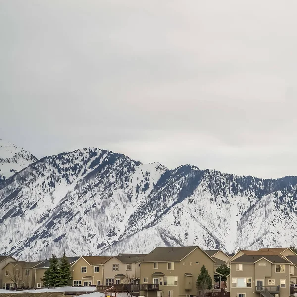 Marco cuadrado Sorprendente montaña cubierta de nieve y casas de varios pisos bajo cielo nublado — Foto de Stock