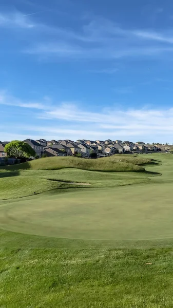 Pionowe pole golfowe z widokiem na piękne domy i góry pod błękitne niebo z chmur — Zdjęcie stockowe