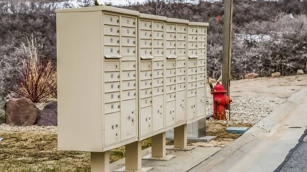 Панорама Белый металлический кластер почтовые ящики и красный пожарный гидрант вдоль бетонной дороги — стоковое фото