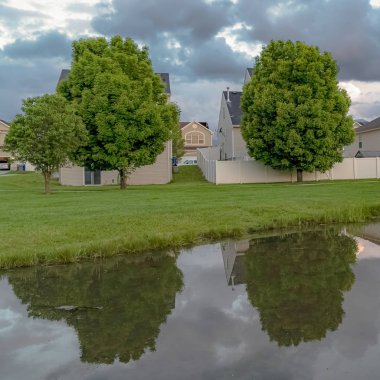 Kare çerçeve Evler ve ağaçlar çimenli bir arazi ortasında bir göletin parlak su yansıyan