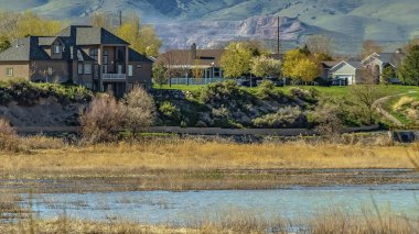 Panorama çerçeve Güneşli bir günde dağ ve soluk mavi gökyüzü manzaralı bir gölün yakınında inşa edilmiş evler