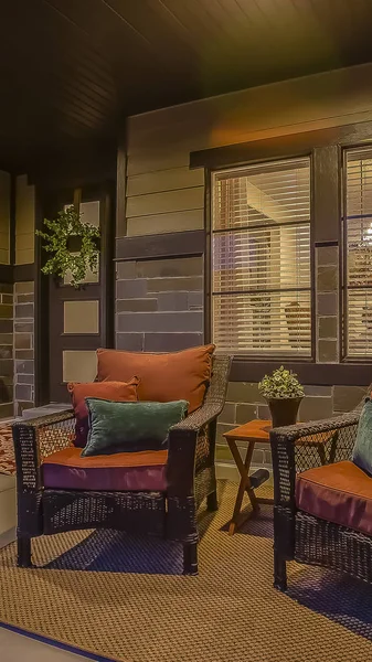 Vertical frame Wicker armchairs on the porch of a home with dark brick wall viewed at night