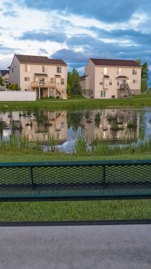 Dikey Dikey Yeşil metal tezgah evleri ve bulutlu gökyüzü yansıması ile parlak bir gölet bakan