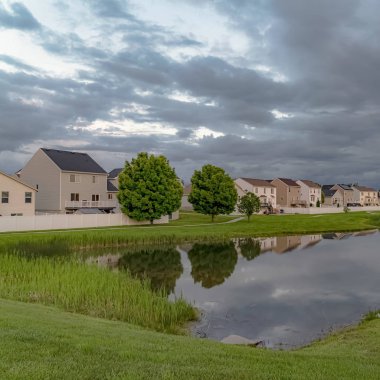 Bulutlu bir gökyüzü altında parlak bir gölet ve yol ile Square Scenic mahalle parkı