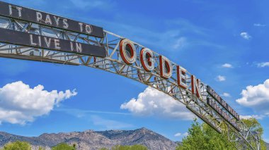 Panorama frame The welcome arch in Ogden Utah against vibrant trees and towering mountain clipart