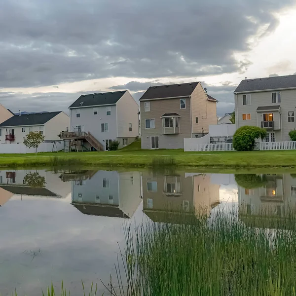 Casas familiares cuadradas y cielo nublado brillante reflejado en el brillante estanque del barrio — Foto de Stock