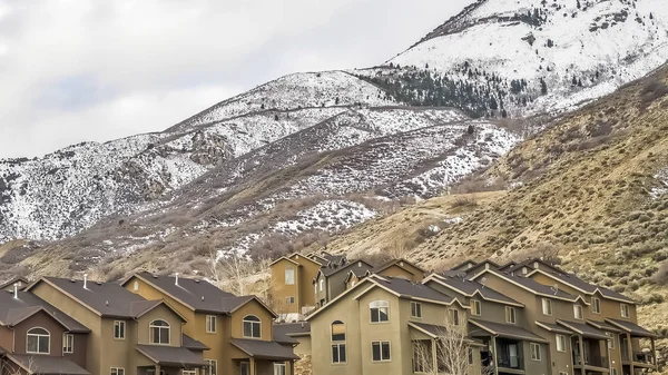 Panorama Casas contra una montaña cubierta de nieve y cielo azul lleno de nubes gruesas — Foto de Stock