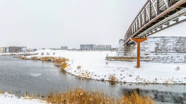 Marco panorámico Lago y edificios rodeados de suelo nevado bajo el cielo nublado en invierno — Foto de Stock