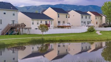 Balkonlu evlerin önünde çimenli bir arazinin ortasında Panorama Parlak gölet ve patika