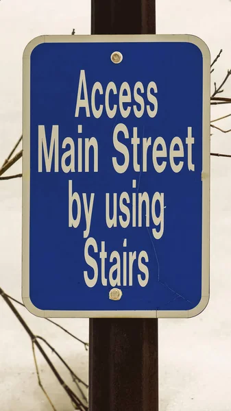 Vertikale Nahaufnahme eines blauen Schildes, das den Zugang zur Hauptstraße über eine Treppe beschreibt — Stockfoto