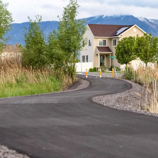 Square Winding road leading to distant homes with mountain and cloudy sky background — Stock Photo, Image