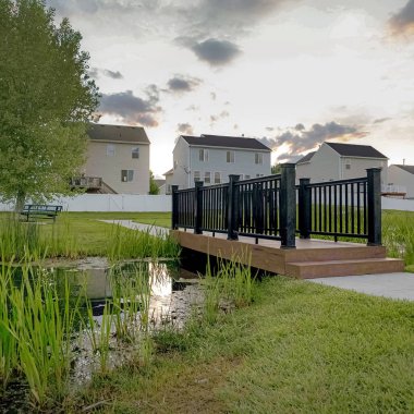 Gün batımında bir ağaç evler ve coudy gökyüzü manzaralı küçük bir gölet üzerinde Kare çerçeve Köprü