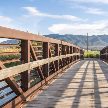 Kare çerçeve Dağ manzaralı bir göl üzerinde metal kafes korkuluk ile Ahşap köprü