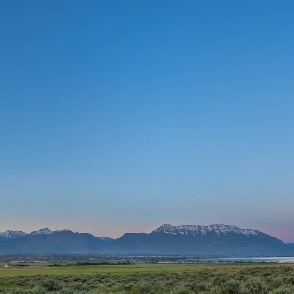 Čtvercový rám malebné panoramatické zobrazení údolí jezera a zasněžené hory pod modrým nebem — Stock fotografie