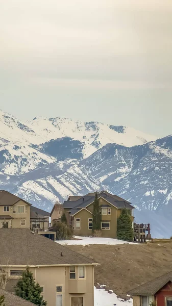 Vertical Vista de invierno de un barrio en una colina contra la montaña y un cielo nublado —  Fotos de Stock