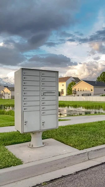 Вертикальный почтовый ящик на обочине дороги на фоне пруда и домов — стоковое фото