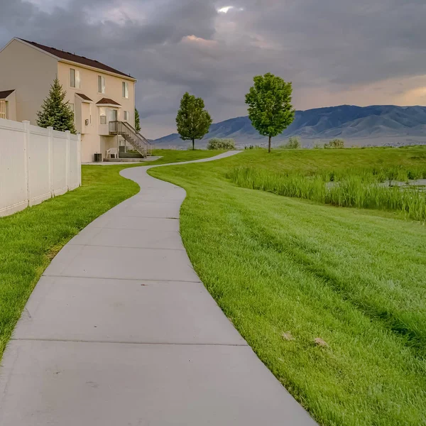 Square Paved walkway in front of homes with view of a pond and vast grassy terrain