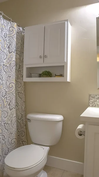 Vertical Toilet vanity mirror and cabinet inside bathroom with beige wall and tile floor