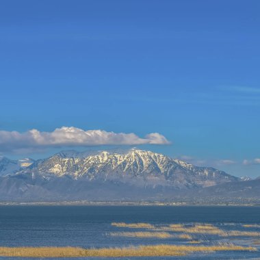 Kar tepeli dağ ve sakin göl üzerinde kabarık bulutlar ile Canlı mavi gökyüzü