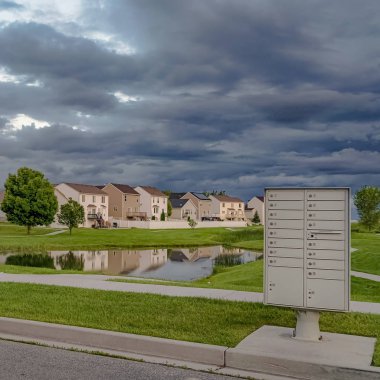 Kare çerçeve Gökyüzü geniş bir çimenli arazi ortasında evler ve gölet üzerinde gri bulutlar ile dolu