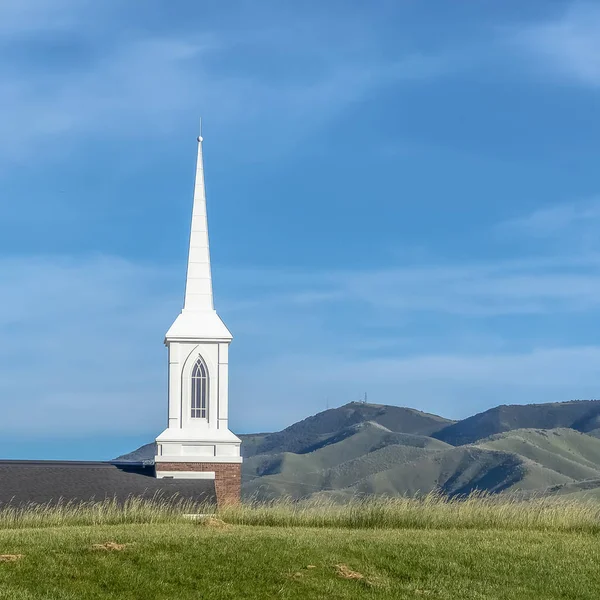 Marco cuadrado campanario blanco y azotea de una iglesia vista desde una colina cubierta de hierba en un día soleado — Foto de Stock