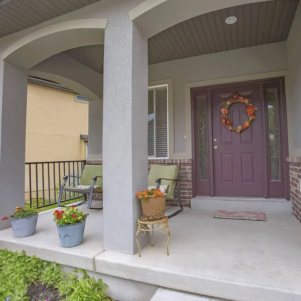 Square Home facade with rocking chairs and potted flowers on the concrete porch