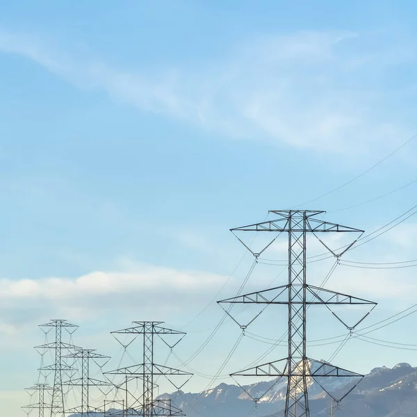 Square tornar kraftledningar i dalen mot snötäckta berg och blå himmel — Stockfoto