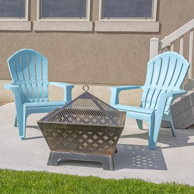 Güneşli bir günde bir evin bahçesinde Kare ateş çukuru ve mavi plastik sandalyeler