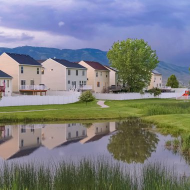 Kare çerçeve Balkonlu evlerin önünde çimenli bir arazi ortasında parlak gölet ve patika