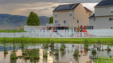 Panorama Oyun alanlarının yansıması ile parlak çimenli gölet bulutlu gökyüzü ve çit