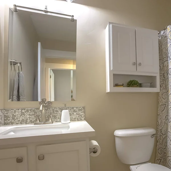 Square Toilet vanity mirror and cabinet inside bathroom with beige wall and tile floor