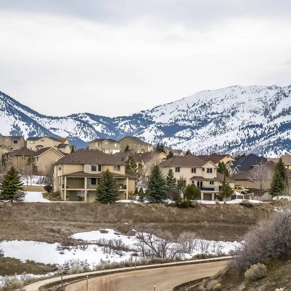 Marco cuadrado Camino pavimentado curvado a través de la colina nevada con casas de varios pisos en la distancia — Foto de Stock