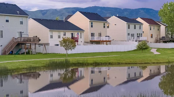 Balkonlu evlerin önünde çimenli bir arazinin ortasında Panorama Parlak gölet ve patika