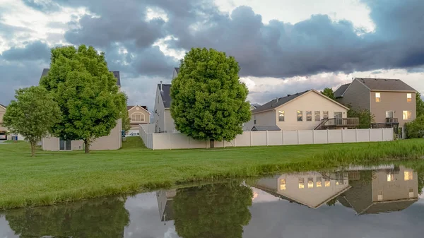 Panorama Evleri ve ağaçlar çimenli bir arazi ortasında bir göletin parlak su yansıyan