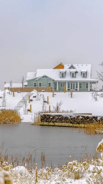 Vertical Vista panorámica de invierno de un lago tranquilo con una hermosa casa cerca de la orilla nevada — Foto de Stock