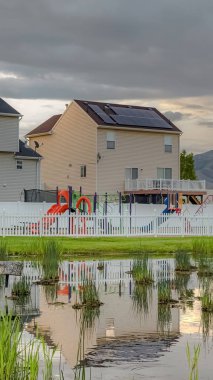 Dikey çerçeve Oyun evleri bulutlu gökyüzü ve çit yansıması ile Parlak çimenli gölet