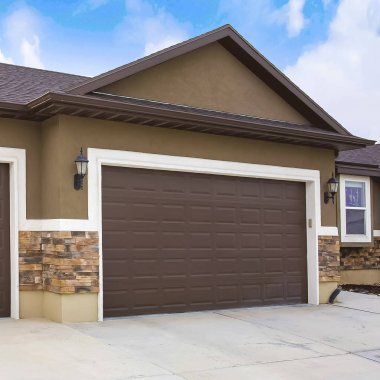 Bulutlu mavi gökyüzüne karşı iki kahverengi garaj kapıları ile bir evin dış