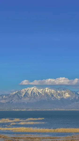 Cielo azul vivo vertical con nubes hinchadas sobre una montaña nevada y un lago tranquilo —  Fotos de Stock