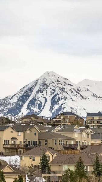 Marco vertical Casas de colina con escarpado pico de montaña cubierto de nieve en el fondo — Foto de Stock