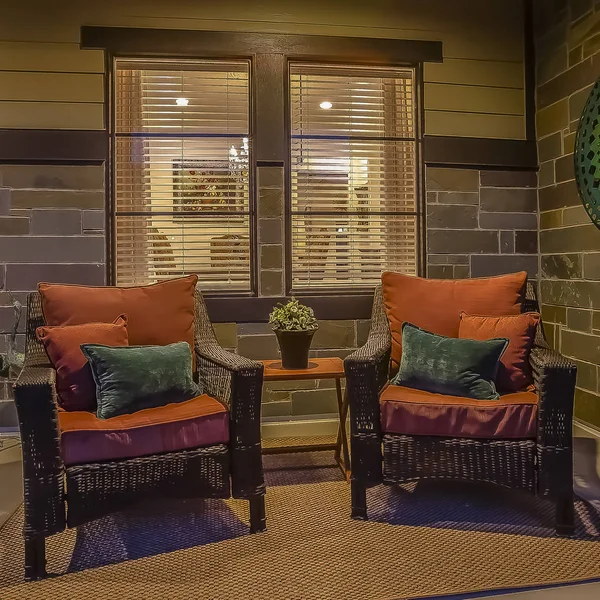 Square frame Wicker chairs and table at the cozy porch of a home viewed at night