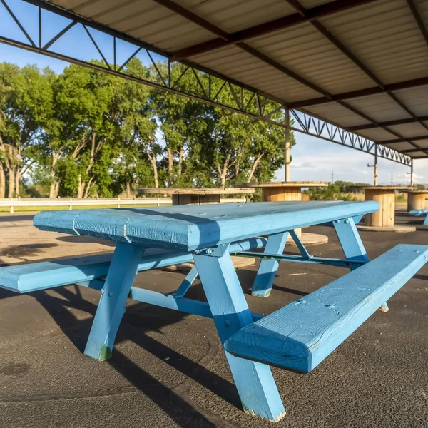 Square frame Blue picnic tables with seats and spool tables under a pavilion on a sunny day