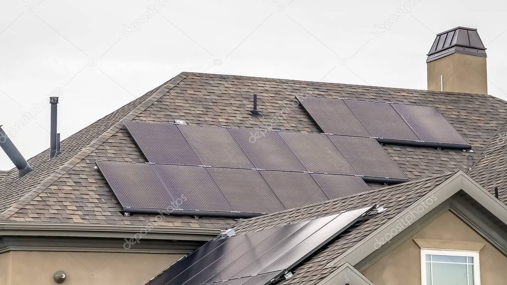 Panorama Solar panels on the dark pitched roof of a home with cloudy sky background