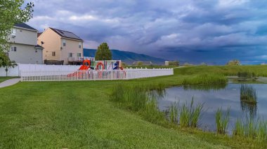 Panorama Tezgah ve arka planda oyun alanı ve evleri ile çimenli bir parkta gölet