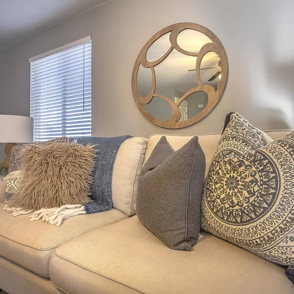 Square frame Sofa with fluffy pillows inside a living room with round mirror and gray wall