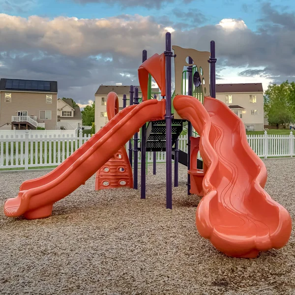 Square frame Neighborhood playground with bright colorful slides and swings under cloudy sky