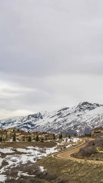 Vertical Curvy estrada e casas construídas em uma colina com vista para a montanha coberta de neve imponente — Fotografia de Stock