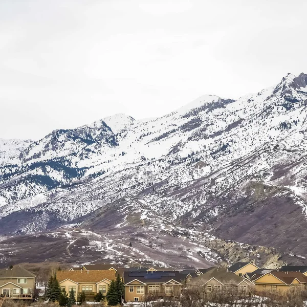 Quadro quadrado Área residencial na base de uma montanha nevada imponente contra o céu nublado — Fotografia de Stock