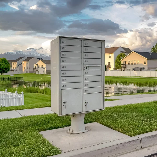 Квадратный почтовый ящик на обочине дороги на фоне пруда и домов — стоковое фото