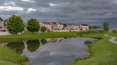 Bulutlu bir gökyüzü altında parlak bir gölet ve yol ile Panorama Manzara mahalle parkı