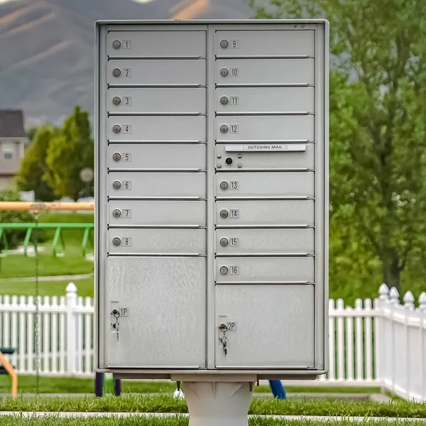 Fyrkantig ram vit metall Cluster brevlåda på trottoaren framför en färgglad lekplats — Stockfoto